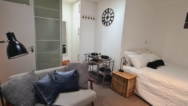 A compact bedroom with a bed, a small desk with a chair, a sofa with cushions, a lamp, and a wardrobe. - Maple House - Inviting 1-bed Apartment in London (London)