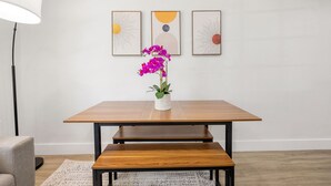 Een eettafel met een bankje, een bloempot en drie ingelijste kunstwerken aan de muur.