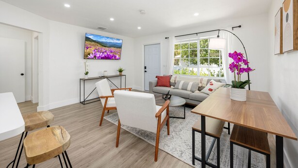 Een moderne woonkamer met een bank, stoelen, een salontafel en een aan de muur bevestigde televisie.