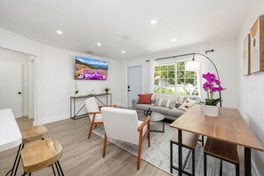 Een moderne woonkamer met een bank, stoelen, een salontafel en een aan de muur bevestigde televisie.