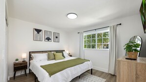 Een slaapkamer met een bed, nachtkastje, lamp en een raam met gordijnen.