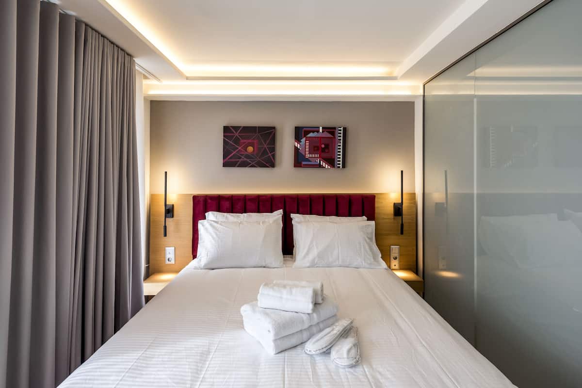 Una camera d'albergo moderna con un letto rifatto, due opere d'arte appese al muro e una testiera rossa.