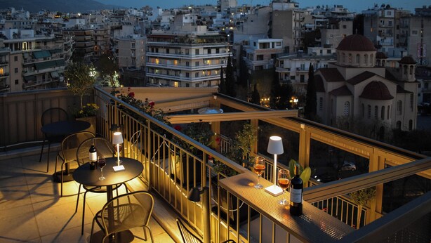 Una terraza en la azotea con mesas y sillas, vista panorámica de la ciudad y un edificio con cúpula.