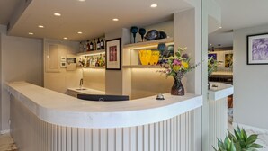 Una moderna zona de recepción con un mostrador curvo, un lavabo y un jarrón con flores. Hay estanterías con botellas y obras de arte enmarcadas.
