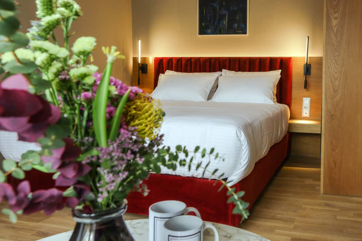 Una camera d'albergo con un letto, un vaso di fiori e un tavolo con due tazze.