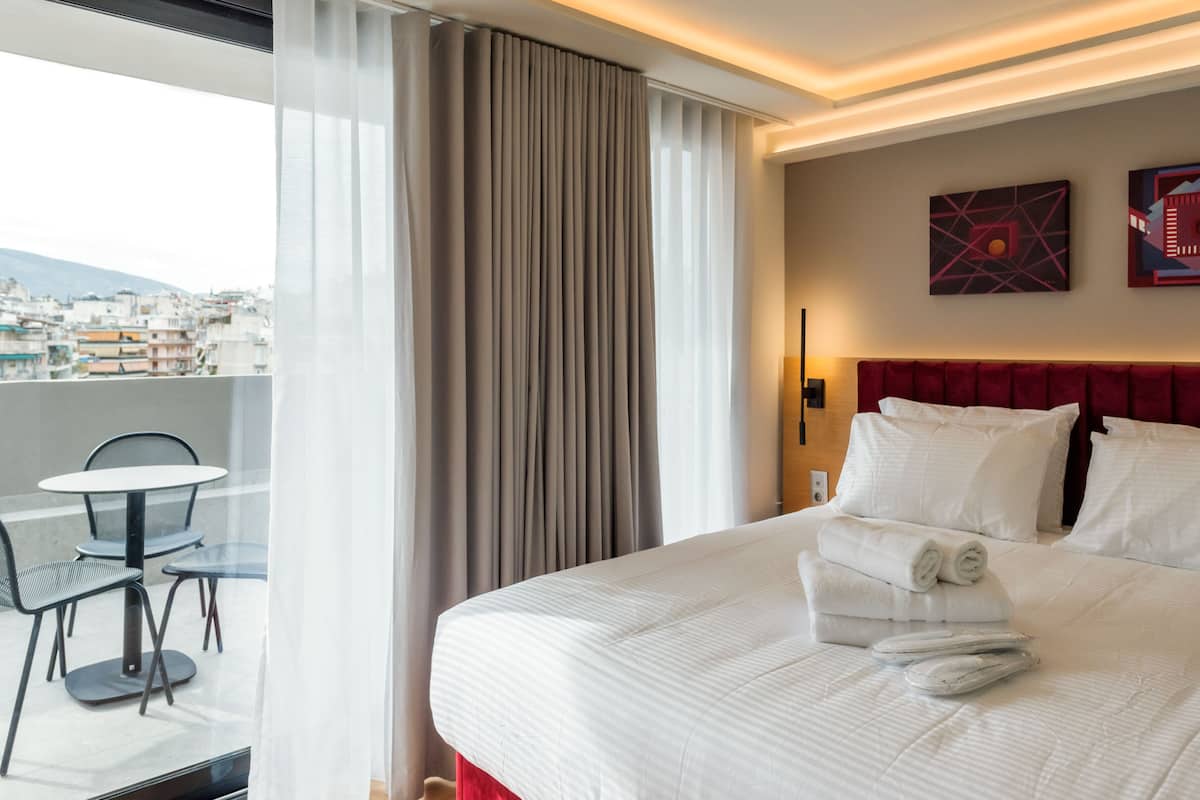 Camera d'albergo con un letto grande, una testiera rossa e vista sulla città attraverso una finestra con tende.