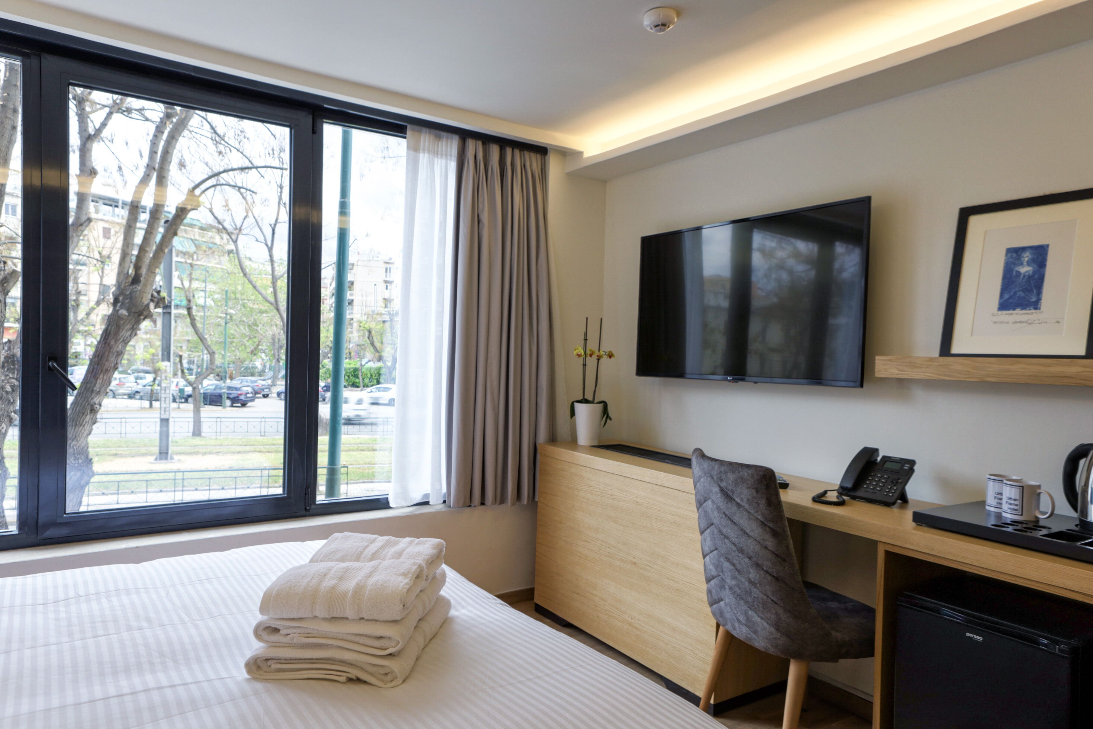 A hotel room with a bed, a desk with a chair, a television, and a window with curtains.