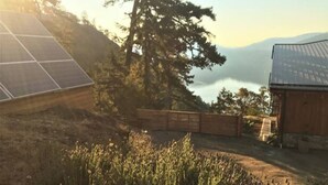 A solar panel, a wooden fence, and a building with a sloped roof. - Two-Bed Cabin – Breathtaking Fjord View at the Summit House. (Malahat)