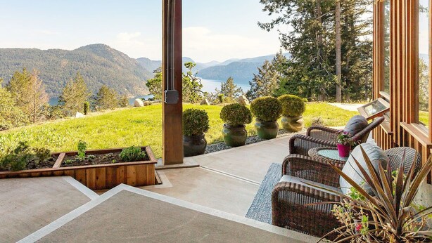 A patio with wicker furniture, a view of mountains and a lake, and a wooden pergola. - Panoramic Suite  – Breathtaking Fjord View, Summit House. (Malahat)