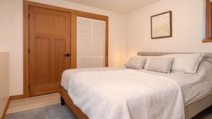 A bedroom with a bed, a wooden door, a closet with louvered doors, and a framed picture on the wall. - Panoramic Suite  – Breathtaking Fjord View, Summit House. (Malahat)
