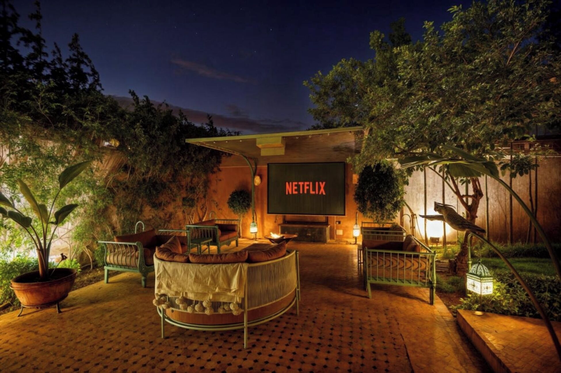 Zona d'estar exterior amb cartell de Netflix, un foc i plantes en testos.