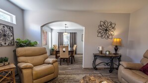 A living room with a beige sofa, a coffee table with decorative items, a dining area with a table and chairs, and a decorative wall piece. - Spacious 3 bedroom 2.5  bath with 3 living areas (Las Cruces)