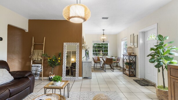 Amplia sala de estar con un sofá marrón, un comedor con mesa y sillas, y una zona de cocina con mostrador y taburetes.