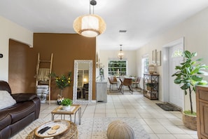 A spacious living room with a brown sofa, a dining area with a table and chairs, and a kitchen area with a counter and stools.