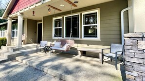 Ein Haus mit Veranda, einer Schaukel, einer Bank und einer Steinmauer.