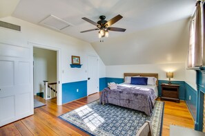 Un dormitorio con cama, mesita de noche, ventilador de techo y vista a una escalera.