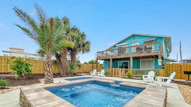 A turquoise two-story house with a balcony, a swimming pool, and white Adirondack chairs. - DOG-FRIENDLY, OUTDOOR POOL, DUPLEX BEACH HOUSE!! (Gulf Shores)