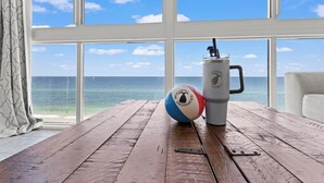 Taula de fusta amb una pilota de platja i una tassa, a prop d'un gran finestral amb vista a l'oceà.