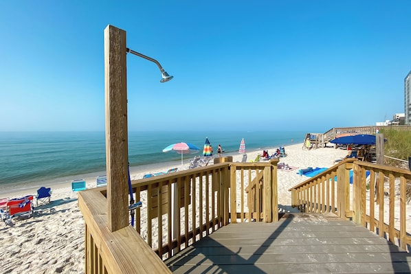 A wooden deck leading to a beach with beach chairs and umbrellas.