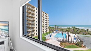 Une pièce dotée d’une grande fenêtre donnant sur une piscine et sur un immeuble avec des balcons.