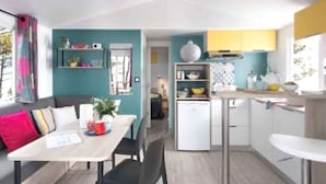 A compact living space with a kitchenette, a dining area, and a small seating area. - Camping familial 4* | Mobil-home + Accès piscine (Monterblanc)