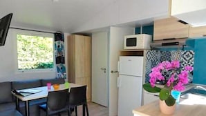 A compact kitchen with a microwave, refrigerator, and a small dining area with a table and chairs. - Camping familial 4* | Mobil-home + Accès piscine (Monterblanc)