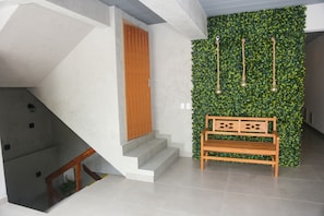 A modern interior with a staircase, a wooden door, a bench, and a wall with hanging lights.