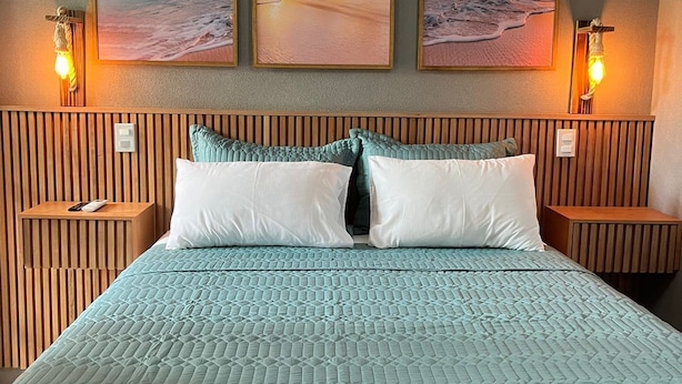 A hotel room with a large bed, wooden headboard, and three framed beach sunset pictures on the wall. - Palulu Flats (São Sebastião)
