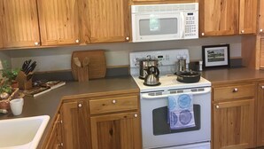 Une cuisine avec des meubles de rangement en bois, un four à micro-ondes blanc, une cuisinière et divers ustensiles de cuisine.