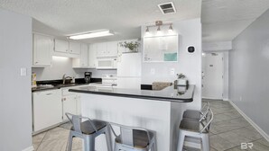 Une cuisine moderne avec des meubles blancs, un grand îlot central doté de tabourets, un four à micro-ondes et une machine à café.