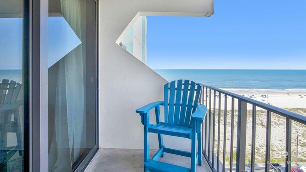 Un balcon avec vue sur la plage, une chaise bleue et une porte vitrée.