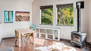Una sala de estar moderna con una mesa de comedor de madera, sillas amarillas, un mueble de almacenamiento blanco y una estufa a leña.