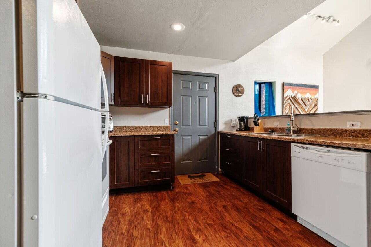 Una cocina compacta con armarios de madera oscura, un refrigerador blanco y un lavavajillas.