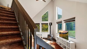 Amplia sala de estar con techo alto, chimenea y ventanas grandes que ofrecen vistas al exterior.