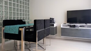 A modern room with a dining table, chairs, a coffee machine, and a flat-screen TV on a stand.
