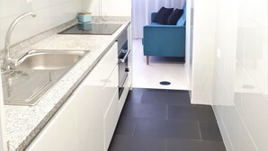 A compact kitchen with a double sink, a countertop, and a small window with curtains.