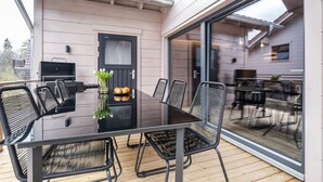 Un espace extérieur aménagé pour les repas, avec une table et des chaises en verre, un barbecue et une porte dotée d’une vitre en verre dépoli.