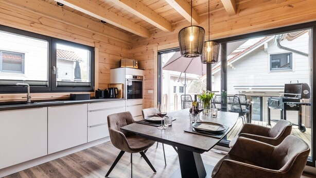Une cuisine moderne avec des poutres en bois, un coin repas avec une table et des chaises, et une vue sur l’extérieur.