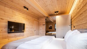 Une pièce de type cabane en bois, avec un lit, un téléviseur fixé au mur et une porte donnant sur une autre pièce.