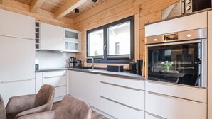 Une cuisine moderne avec des meubles blancs, un four en acier inoxydable et une fenêtre équipée de stores.