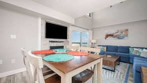 Un salon moderne avec un canapé bleu, une table basse en bois et une table à manger agrémentée de sets de table colorés.