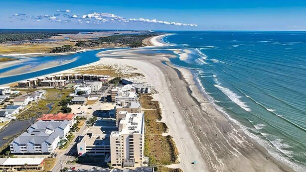 Une vue aérienne d’une zone côtière avec une plage, des bâtiments et un ciel dégagé.