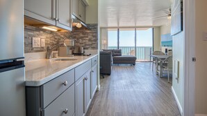 Una cucina moderna con mobili grigi, un piano di lavoro in marmo e una parete rivestita in pietra. C'è una zona pranzo con tavolo e sedie, e un balcone con vista.