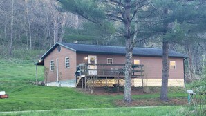 Une maison en bois d’un seul étage, dotée d’un porche, entourée d’un champ verdoyant et d’arbres.