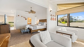 Een moderne slaapkamer met een bed, een bank, een bureau en een groot raam met uitzicht op gebouwen en palmbomen.