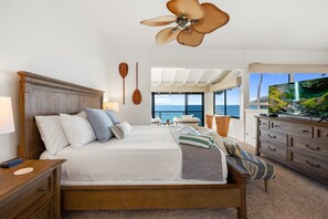 A bedroom with a wooden bed, a ceiling fan, a view of the ocean, and a wooden dresser. - 2bd endless luxury, and soothing sounds of waves (Lahaina)