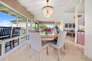 A spacious dining area with a glass table, wicker chairs, and a chandelier. - 2bd endless luxury, and soothing sounds of waves (Lahaina)