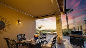 Une terrasse extérieure avec une table et des chaises, un barbecue et une vue sur le coucher de soleil.