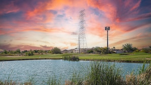 Un terrain de golf avec un plan d’eau, un pylône électrique imposant et des maisons résidentielles en arrière-plan.