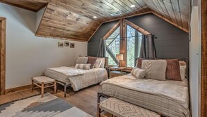A cozy bedroom with two beds, wooden flooring, and a sloped ceiling. - Whiskey Hollow Lodge - Mountain Views | Outdoor Living | Hot Tub (Morganton)